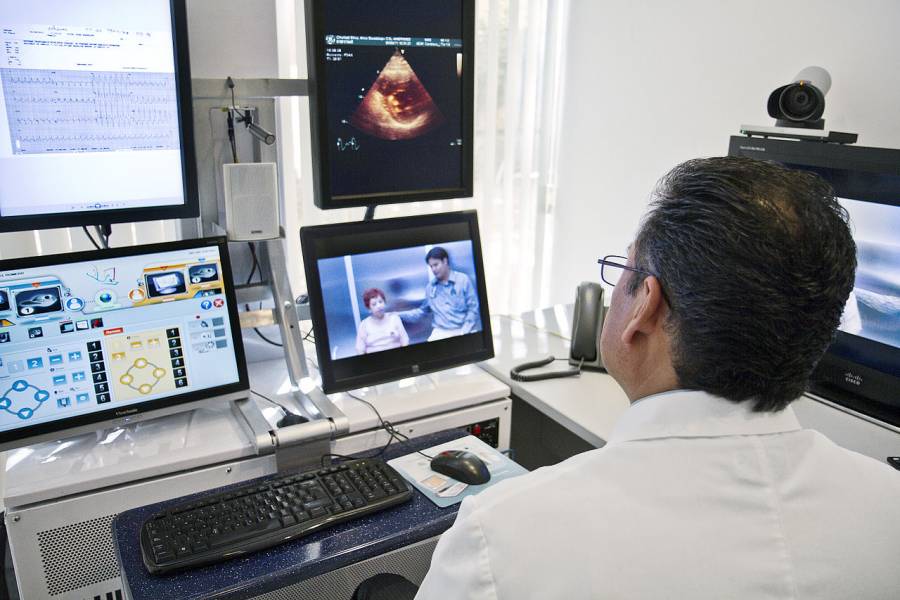 A healthcare provider talks to a patient via video chat while seeing image scans and test results in various screens.