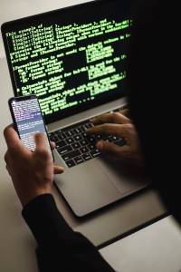 A silhouetted man sits in front on a laptop on his phone. This is a stock image for an article on a crypto scam.