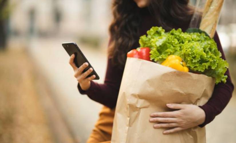 A woman checking her phone while holding a bag of groceries.