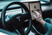 Image of a driver sat behind the wheel of Tesla adjusting the control panel. Tesla have recently announced a recall of most the US models sold