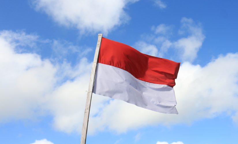 Photo of the Indonesian flag waving in front of a blue, cloudy sky