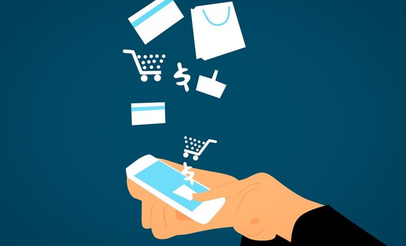 An image depicting ecommerce. A pair of hands hold a mobile phone and shopping icons like a dollar sign and a trolley float up from the screen