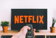 A picture of a person pointing a remote at a tv screen with the Netflix logo on it.