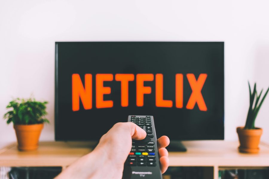 A picture of a person pointing a remote at a tv screen with the Netflix logo on it.