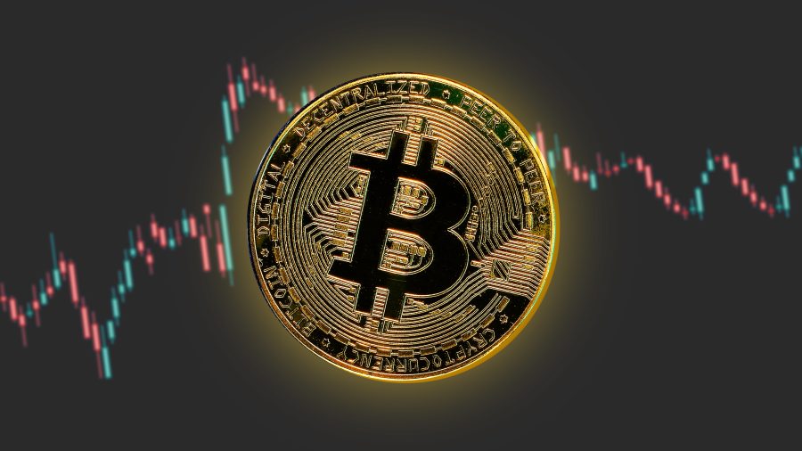 An image of a gold Bitcoin with a candlestick chart in the background.