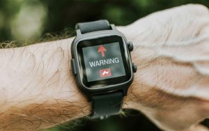a smart watch on a human wrist with a warning sign on the display