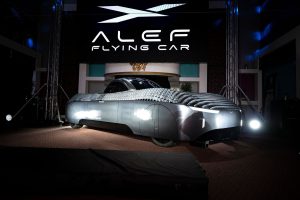 Alef Aeronatic's 'flying car' displayed in a showroom. The car has a white and grey chasis and a black screened central cabin for passengers