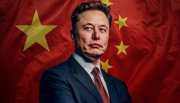 Tesla clears hurdles as it nears self-driving launch in China. The image features Elon Musk in a blue suit with a tie, standing before a backdrop of the Chinese flag, characterized by its large yellow stars against a red field. He has a serious expression, and the portrait seems to convey a sense of formal or official gravity.