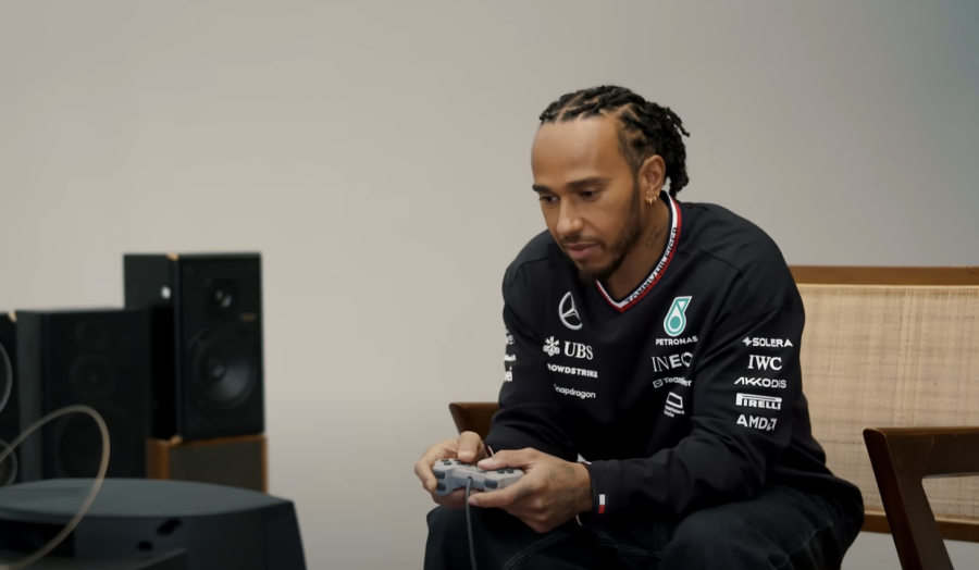 Lewis Hamilton is sitting down playing a PS1 console on a small TV screen.
