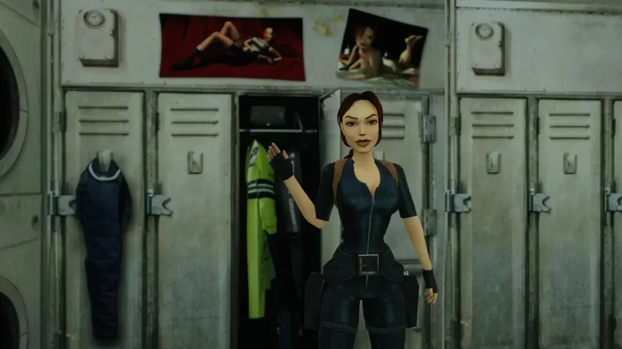 Lara Croft, hero of Tomb Raider III, stands in front of a row of lockers waving her hand, above and behind her are two pinup style images stuck to the walls, showing Croft in provocative pinup-style poses