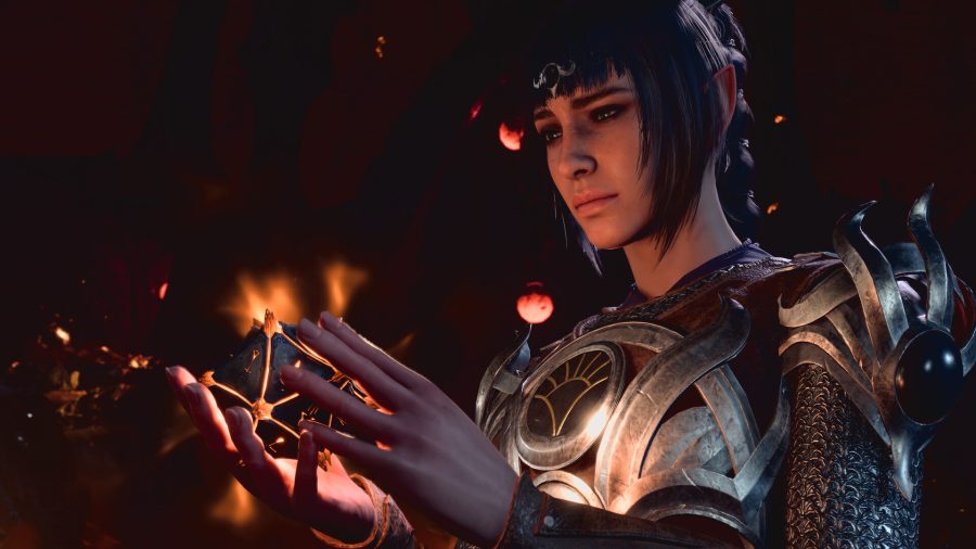 A mage wearing metallic armor gazes into a magical relic, which lights up her face in a soft glow. The image is from Baldur's Gate 3