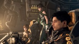 The heroes of Stellar Blade are seen in profile aboard a space vessel which is cast in an eerie green haze. The hero, Eve, is standing.