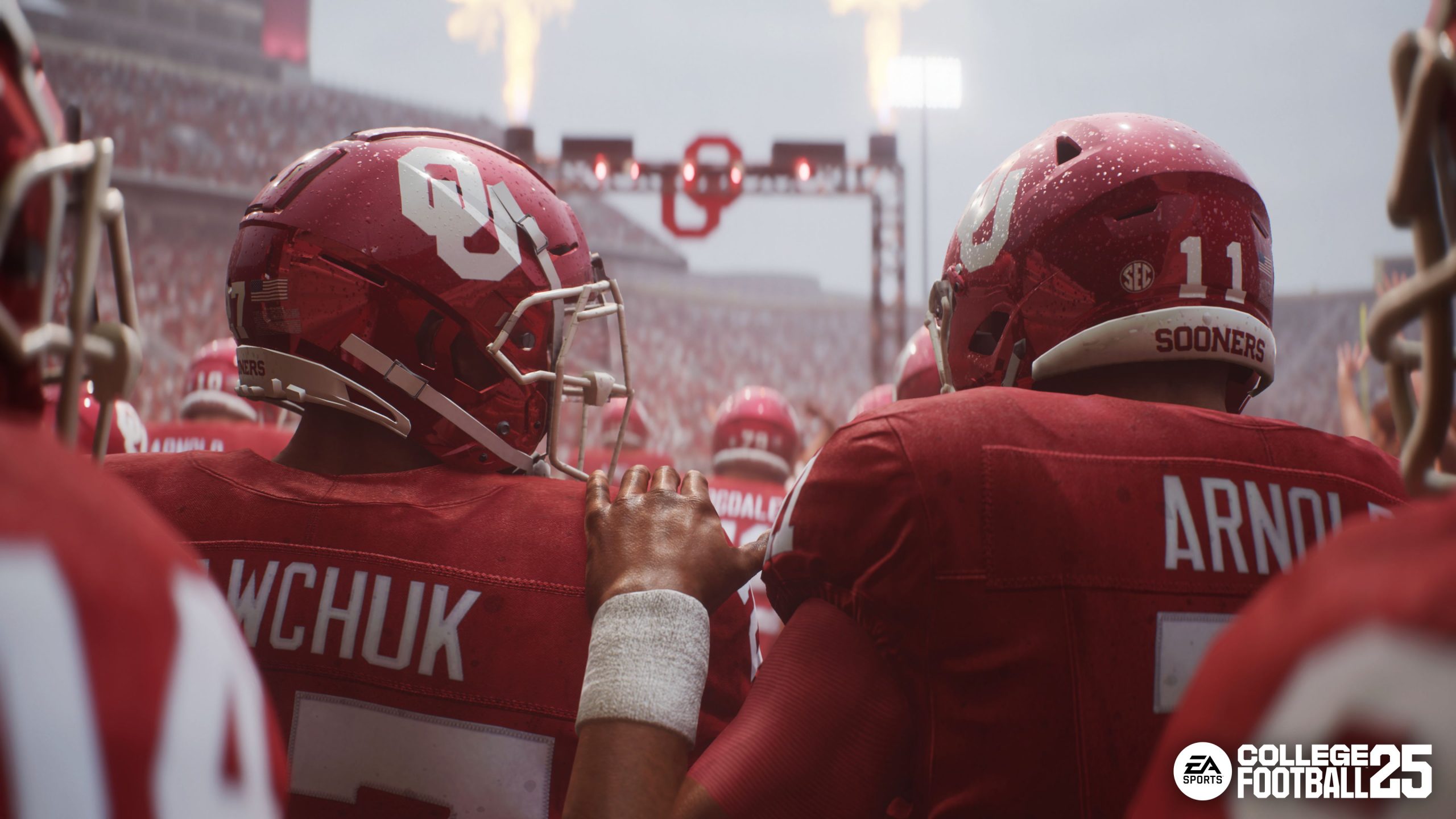 Teammates with the Oklahoma Sooners embrace before taking the field, in the rain, in EA Sports College Football 25. Pyrotechnics detonate in the distance.