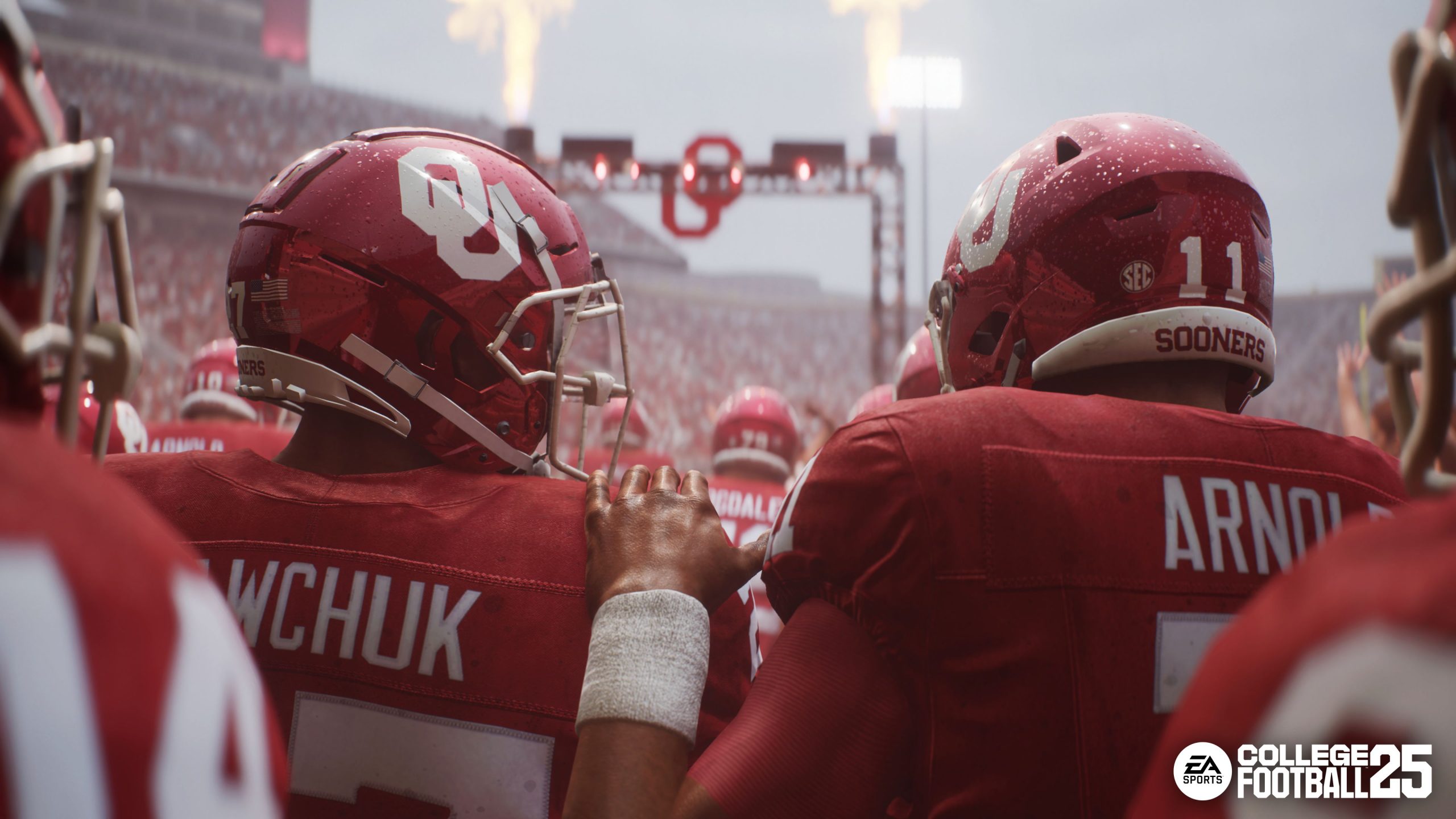 Teamkollegen der Oklahoma Sooners umarmen sich, bevor sie im Regen das Feld betreten, in EA Sports College Football 25. In der Ferne explodiert ein Feuerwerk.