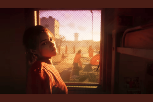 GTA 6 price speculation suggests game may cost more than $70. A woman in an orange shirt looks out through a mesh window, bathed in the warm glow of a sunset. The scene appears to be set in a prison, as suggested by her attire and the secured window. She appears contemplative, her gaze directed outside where other inmates in similar orange outfits can be seen in the yard. The room behind her is modest, indicating the setting of a correctional facility in what could be a scene from Grand Theft Auto VI.