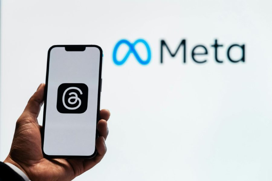 A person holding a mobile phone with the Threads logo infront of a Meta banner