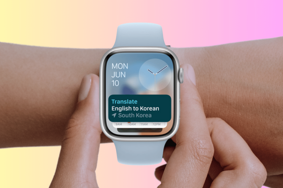 Apple watchOS 11 debuts Translate app but may exclude older models. A close-up image of a person's wrist wearing a smartwatch that displays a translation app. The app screen shows "Translate English to Korean" with "South Korea" indicated below. The background is a soft gradient of pink and yellow, emphasizing the modern and sleek design of the watch and its interface. The date "MON JUN 10" is visible at the top of the smartwatch screen, along with a minimalist time display.