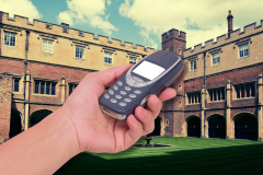 One of U.K.'s top schools bans smartphones, issuing Nokia 'brick' phones instead. A hand holding a Nokia 'brick' phone in front of Eton College, showcasing the school's new policy banning smartphones on campus.
