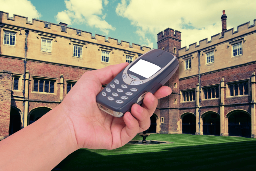 One of U.K.'s top schools bans smartphones, issuing Nokia 'brick' phones instead. A hand holding a Nokia 'brick' phone in front of Eton College, showcasing the school's new policy banning smartphones on campus.