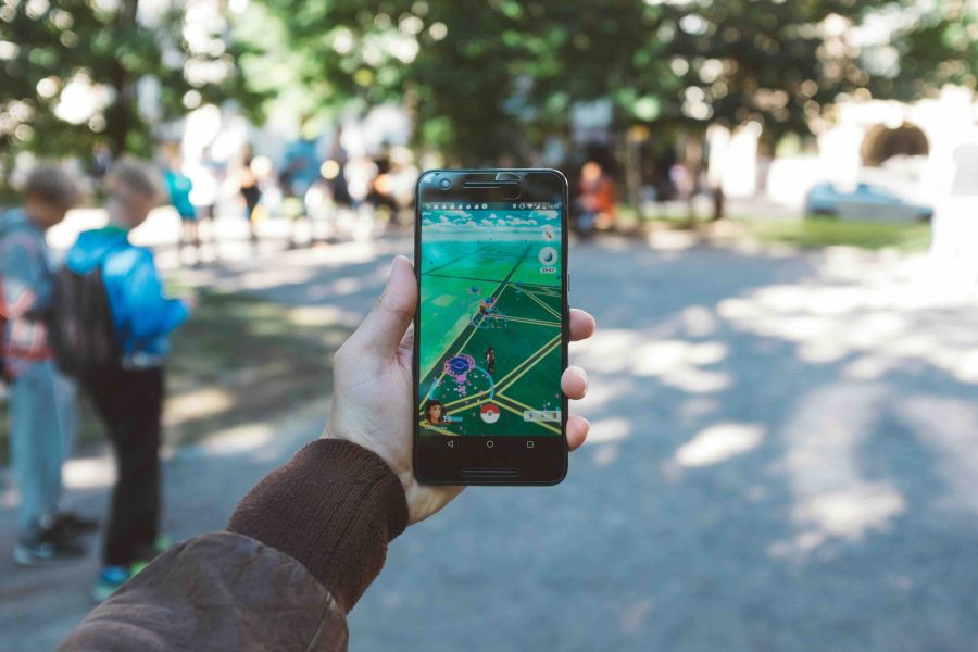 Pokemon Go app on a mobile phone. Someone holding the phone up in a park, can see greenery behind the phone.