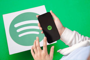 What is Spotify Supremium New lossless tier may be rolled out soon. A person's hands holding a smartphone with the Spotify app open, displayed against a backdrop of a large Spotify logo on a green surface.
