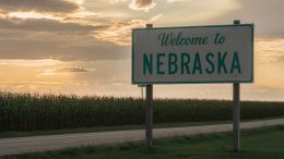 a nebraskan cornfield stretching to the horizon with a "Welcome to Nebraska" road sign in the foreground, cinematic