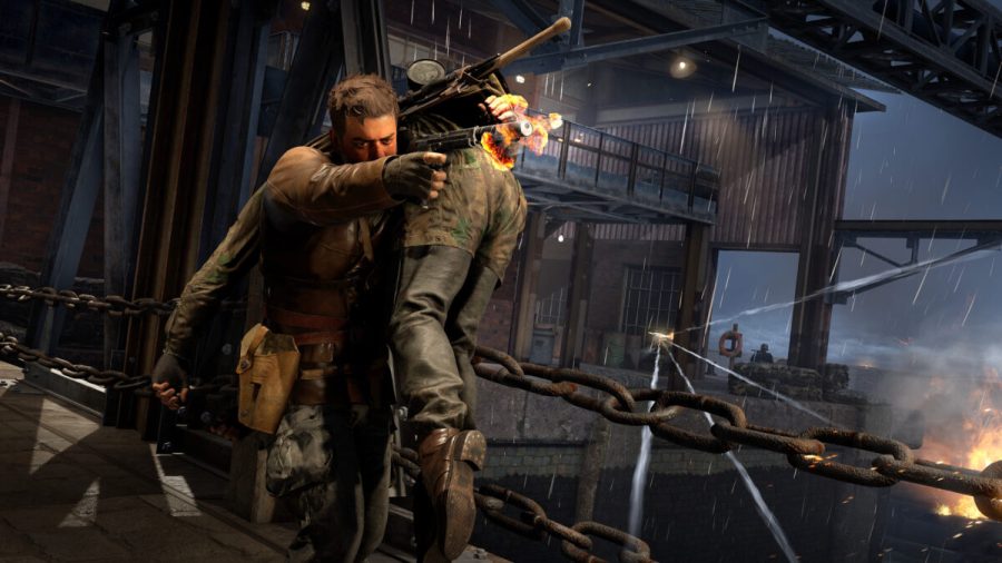 Sniper Elite Resistance's Harry Hawkins has an unconscious Nazi slung over his shoulder while he returns fire with a silenced M1911 pistol in Rebellion Developments' hit game