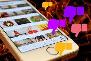 Want ChatGPT to roast your Instagram feed A guide to being insulted by the AI bot. The image depicts a smartphone displaying an Instagram feed surrounded by flames. Overlaid on the screen are multiple thumbs-down icons in various colors, symbolizing strong disapproval or negative feedback on the displayed content.