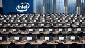 a huge office filled with empty desks, all of which have computers on them. The intel logo is on the wall