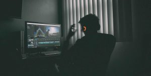 Man working on computer, wearing headphones that are lit up orange.