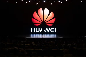 a silhouetted figure standing on a stage with the Huawei logo behind him, the audience is seated stadium style looking down at the stage