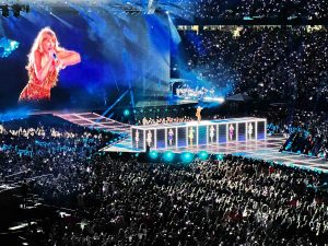 Taylor Swift on stage performing at Gillette Stadium in May as part of the US Era's Tour. She is surrounded by crowds of people and she's on the center of the stage.