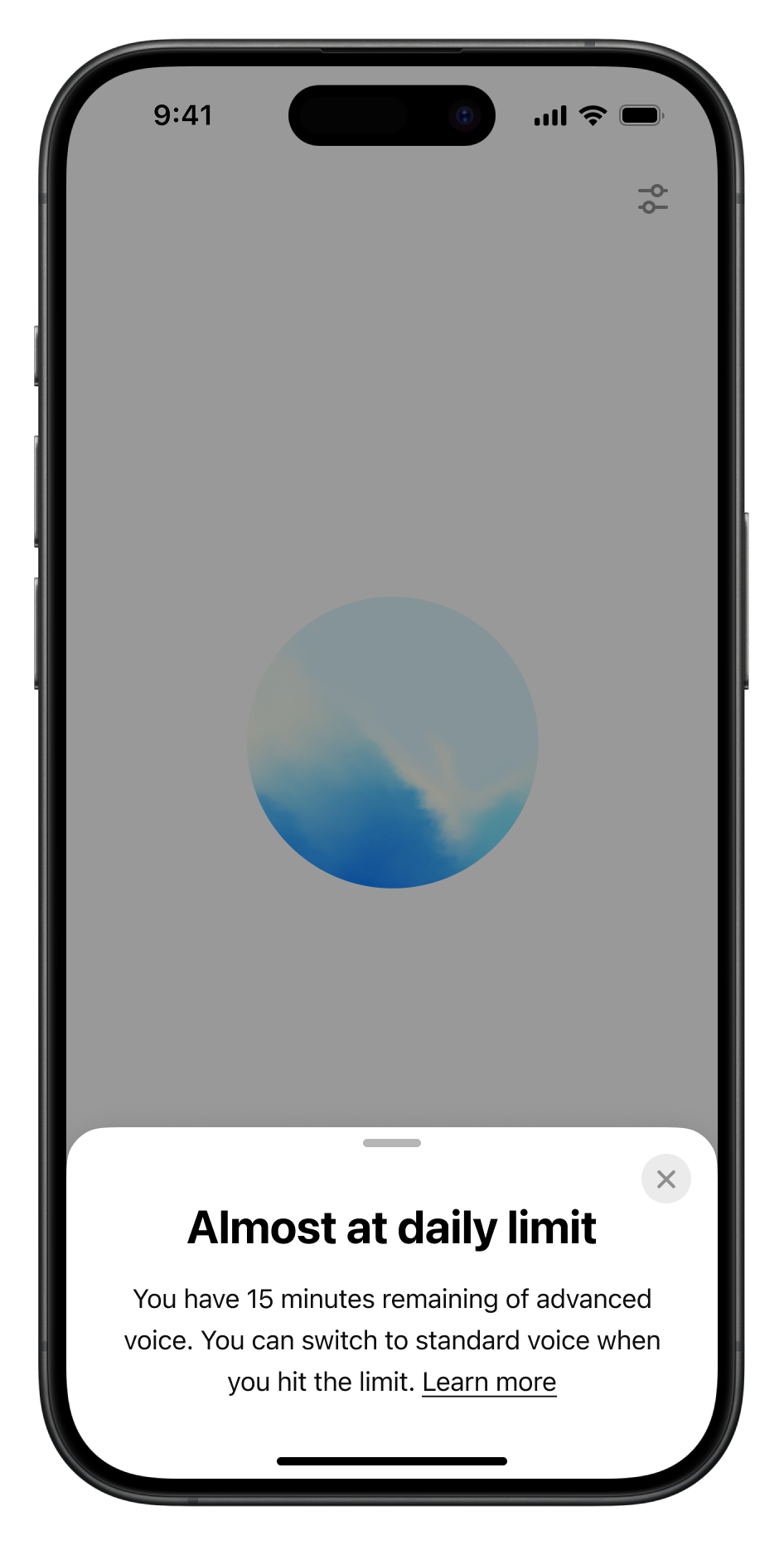 A smartphone screen displaying a notification about nearing the daily limit for advanced voice usage. The message reads, "Almost at daily limit. You have 15 minutes remaining of advanced voice. You can switch to standard voice when you hit the limit. Learn more." A circular blue and white gradient is shown in the middle of the screen, with microphone and settings icons visible at the top.