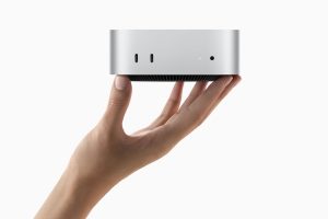 Hand holding up Apple's Mac mini device against a white background.