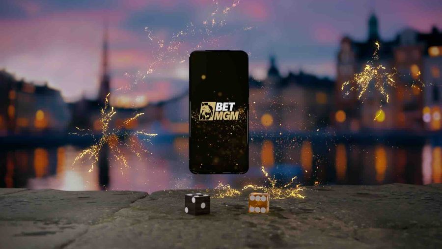 Phone in the centre, with BetMGM logo on it. Two dice are in front and it's on a cityscape backdrop.