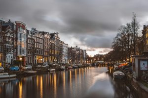 Amsterdam canal with cars parked either side and buildings towering over.