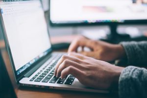 Person writing on laptop, close up. Computer monitor is in the background.