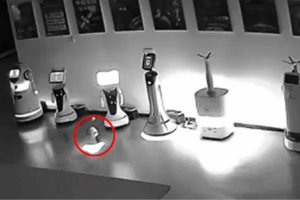 Robot leads 'work revolt' by ordering other bots to 'come home,' sparking unease about AI. Black and white CCTV image of small robot in front of large robots. Small robot is circled in red.