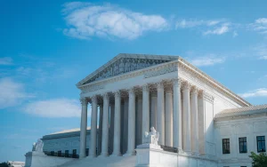 A photo of the Supreme Court building in Washington, D.C. The building is made of white marble and has a large dome. There are columns in front of the building. The sky is clear and blue, with a few clouds.