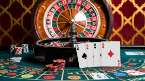 A photo of a casino scene with a roulette wheel in the background. There are cards next to the roulette wheel, and other games such as poker and blackjack are also visible. The background has a red and gold pattern.