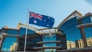 A photo of the Australian flag outside a casino. The flag is flying high against a clear blue sky. The casino building has multiple floors, with glass windows reflecting the surrounding buildings. The building is designed in a modern architectural style.