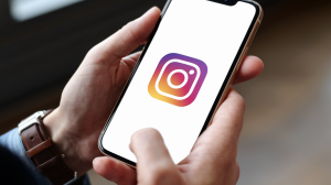 A close-up shot of a person's hands holding a phone. The phone has a blank screen with the Instagram logo in the center.