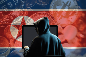 North Korea’s Lazarus Group spreads crypto-stealing malware through open-source software. A hooded hacker sits in front of a laptop, facing away from the viewer. The background features the North Korean flag overlaid with cryptocurrency coins, including Bitcoin. The image symbolizes North Korea’s cyber activities targeting cryptocurrency wallets.