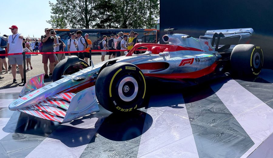 Model of a Formula One car on a stand, with people stood nearby taking photographs.