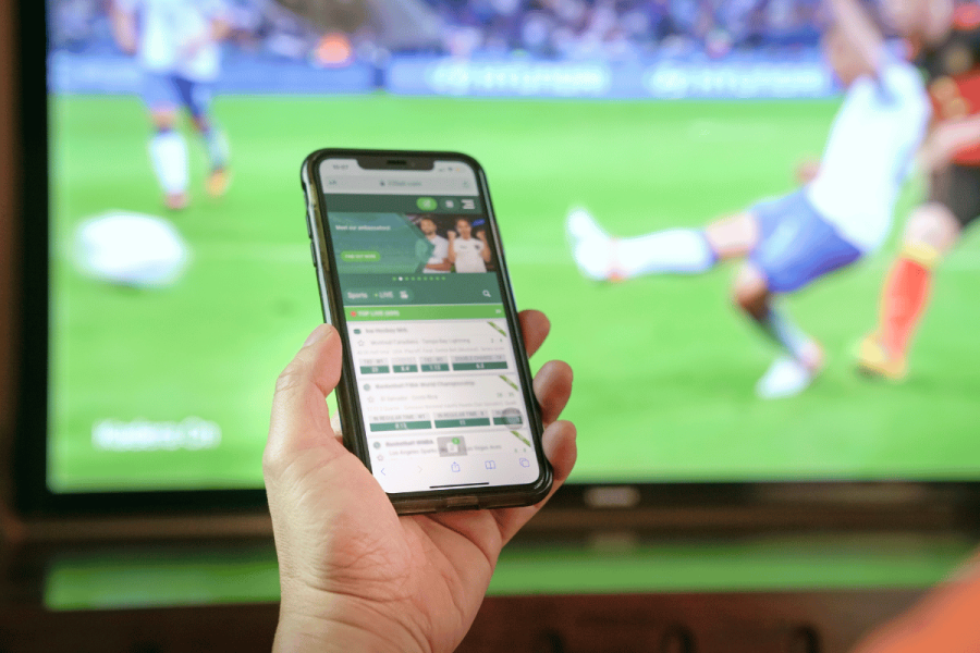 British bookmaker Corbett fined $900K for gambling and money laundering failures. Stock image of person betting on a match using a smartphone.