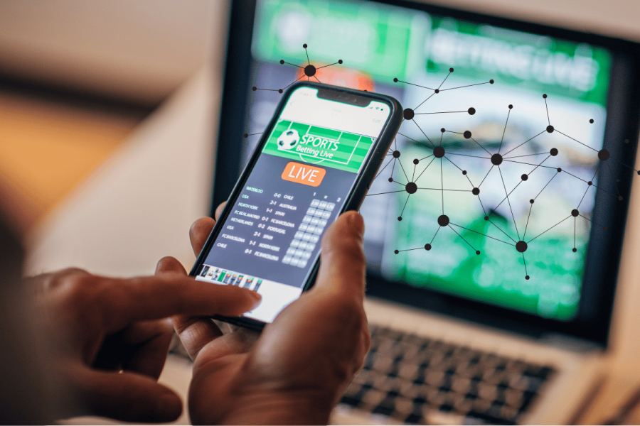 IGSA plans AI best practices framework to guide gambling regulators. A person using a smartphone to access a live sports betting platform, with a laptop screen displaying similar betting content in the background. A digital network overlay symbolizes artificial intelligence and data connections in the gambling industry.