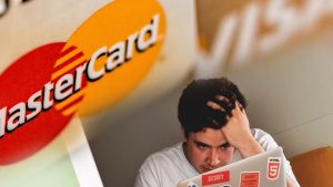 mastercard and visa cards overlayed on top of a man stressed in front of computer