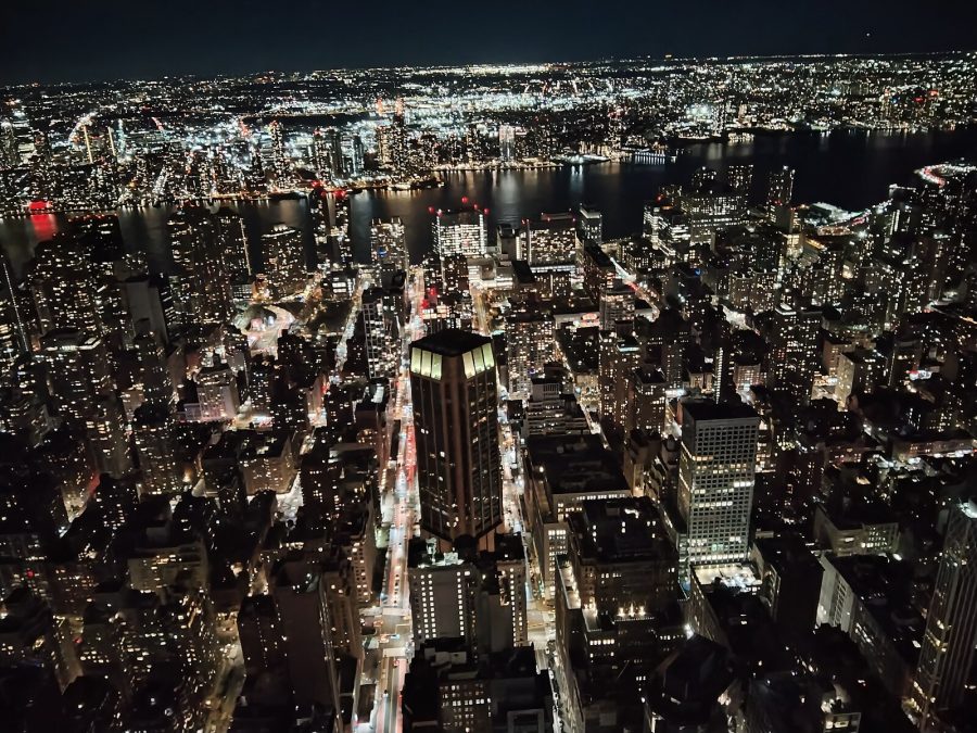 View of New York from the top of the Empire State Building. Can see the glow of the lights and tops of buildings at night time.