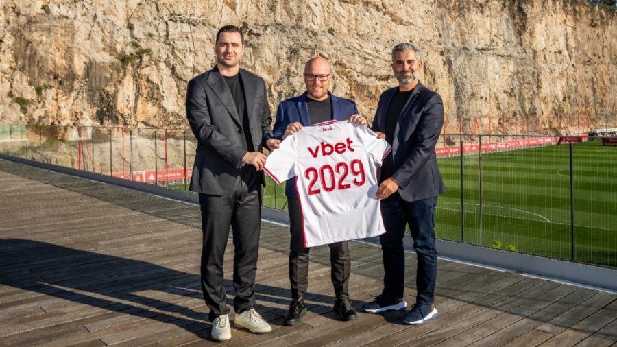 Three people stood close together holding a VBET AS Monaco football shirt.