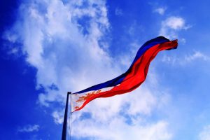 The flag of the Philippines billows in front of a clouded blue sky